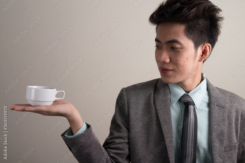 Portrait of young handsome Asian businessman in suit holding coffee cup Portrait of young handsome Asian businessman in suit holding coffee cup