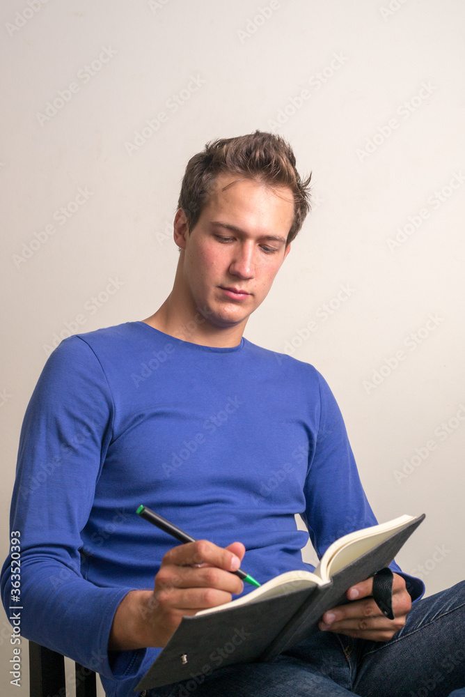Portrait of young handsome man sitting and writing on book Portrait of young handsome man sitting and writing on book