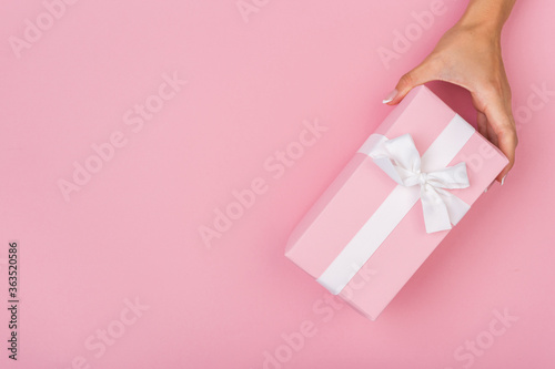 Hands holding craft paper gift box with a gift for Christmas, New Year, Valentine's Day or anniversary on a pink background, top view
