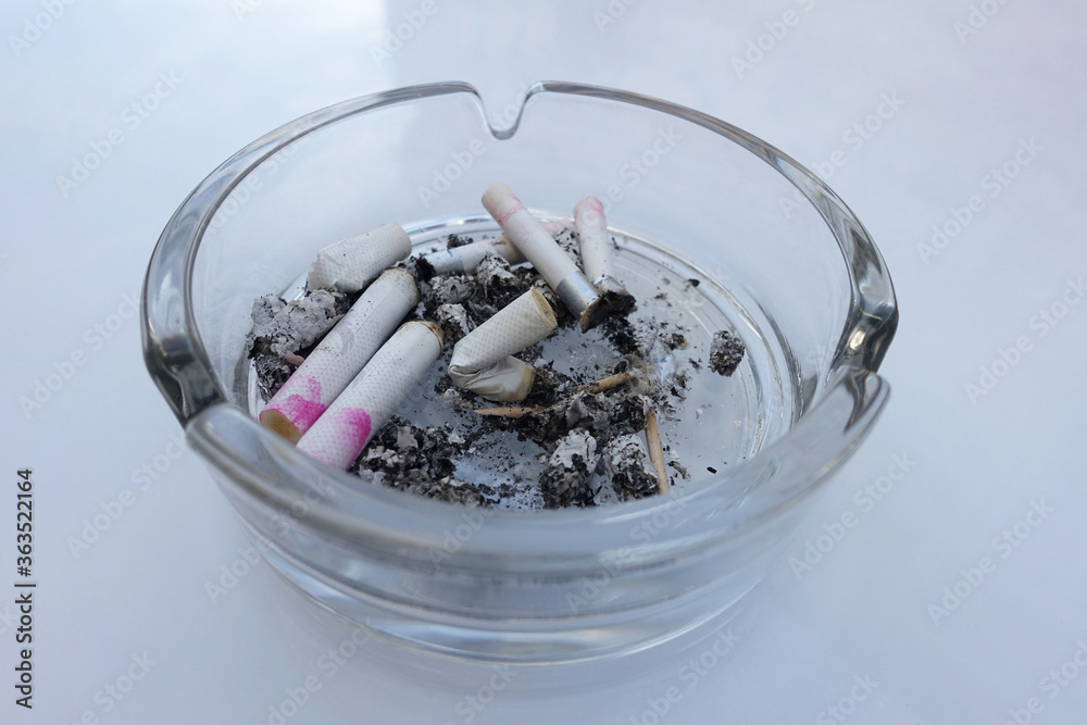 Cigarette stub with pink lipstick in glass ashtray from above. White background. Addiction or hedonism. Cigarette stub with pink lipstick in glass ashtray from above. White background. Addiction or hedonism.