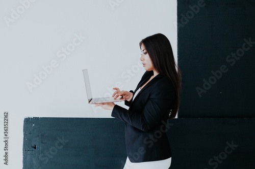 Beautiful brunette woman in white and black business business clothes in the office with a laptop photo