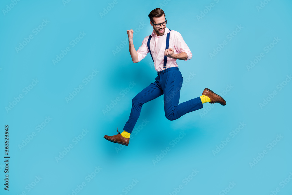 Full size profile photo of handsome man jump high up running competition raise fists first place winner race marathon wear specs shirt suspenders pants boots isolated blue color background Full size profile photo of handsome man jump high up running competition raise fists first place winner race marathon wear specs shirt suspenders pants boots isolated blue color background
