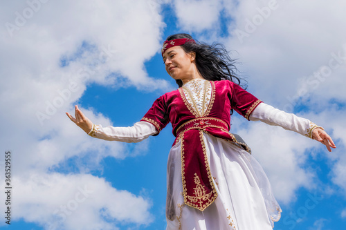 A young girl in an Armenian female national costume dances a bewitching dance against a blue cloudy sky