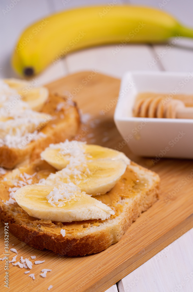 Sandwich with peanut butter, banana, coconut and honey in a bright kitchen. Traditional american breakfast.