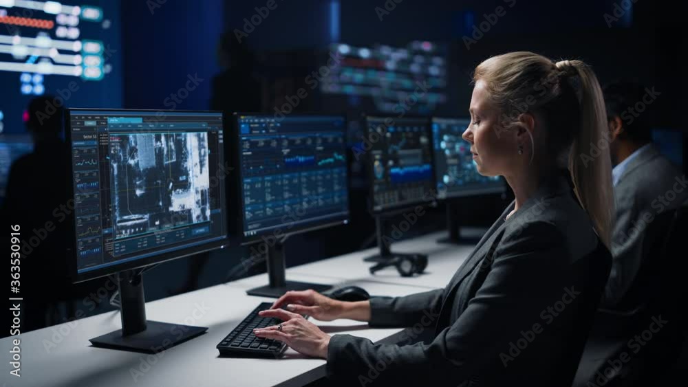 Female Cyber Security Agent Works on Personal Computer Showing Footage of Drone Surveillance Tracking of a Vehicle. Government Surveillance, Safety and Protection Program. System Control Room Female Cyber Security Agent Works on Personal Computer Showing Footage of Drone Surveillance Tracking of a Vehicle. Government Surveillance, Safety and Protection Program. System Control Room
