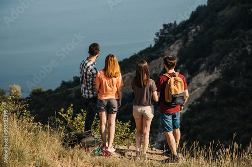 Group of young people hiking in mountains. Tourists with backpacks traveling, standing on a cliff.