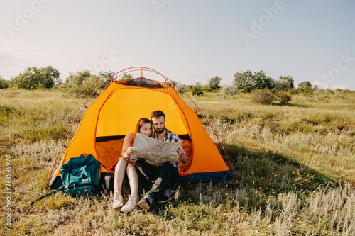 Young couple of man and woman sitting in a tent  looking to a map. Domestic tourism concept.