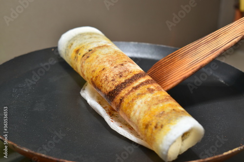 rolling the dosa on hot non stick tawa with wooden spatula