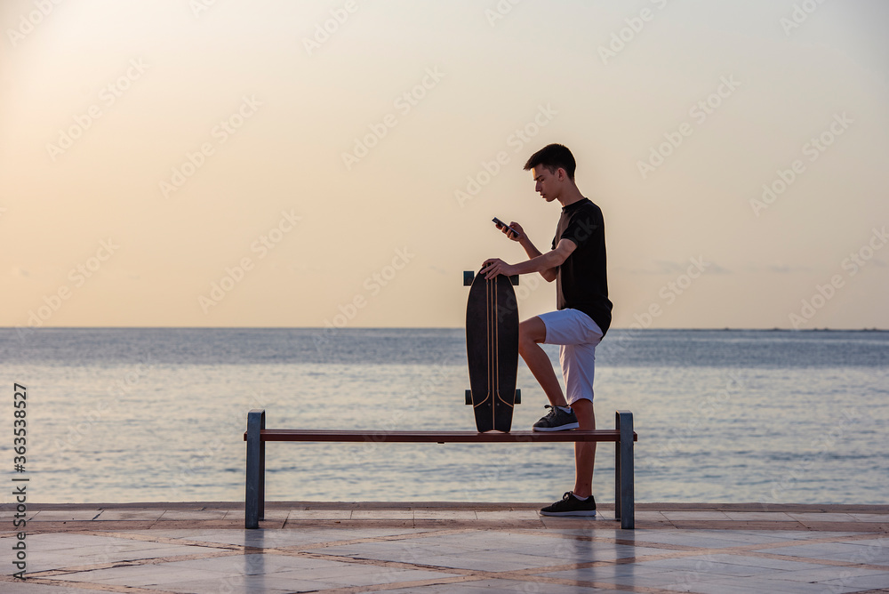 Teenager with his longboard at dawn near the ocean, sea