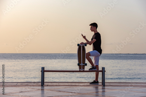 Teenager with his longboard at dawn near the ocean, sea
