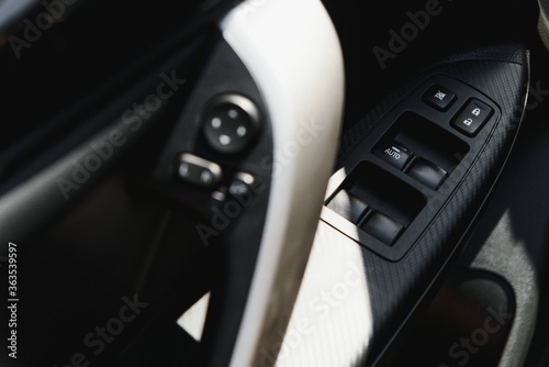 Detail on buttons controlling the windows in a car. Car interior details of door handle with windows controls and electric mirrors adjustments. Car tinted window controls and folding mirror details
