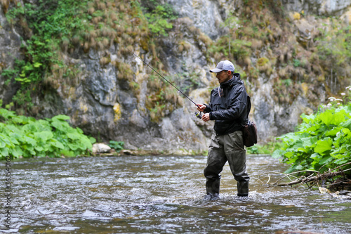 Fisherman hunting salmon fish. Outdoor fishing in river during rain. Hunting and hobby sport.