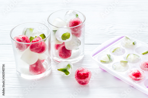 Cocktail glasses with berries in ice cubes on white table