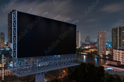 Blank black road billboard with Bangkok cityscape background at night time. Street advertising poster, mock up, 3D rendering. Side view. The concept of marketing communication to promote idea.