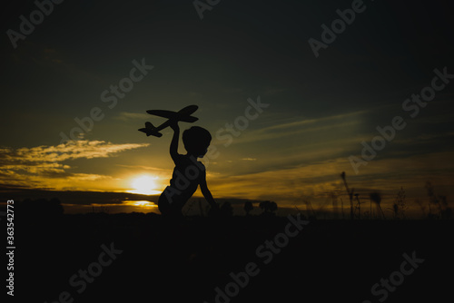 Kid boy playing with toy plane during sunset time. Childhood memories - beautiful sky over meadow. Childhood dream imagination concept