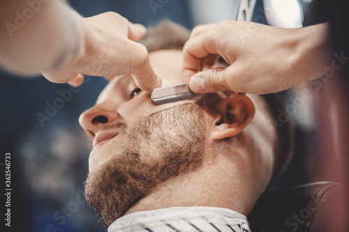 Barber process shaving razor bearded hipster man in barbershop