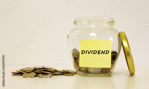 Glass jar with coins for savings. The inscription on the note paper DIVIDEND. Financial concept.