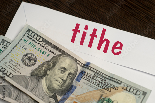 Fotografie White envelope with the inscription tithe and dollar bills lie on a wooden table