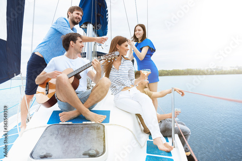 Group of happy friends drinking vodka cocktails at boat party outdoor, cheerful and happy. Young people playing guitar in sea tour, youth and summer vacation concept. Alcohol, vacation, resting.