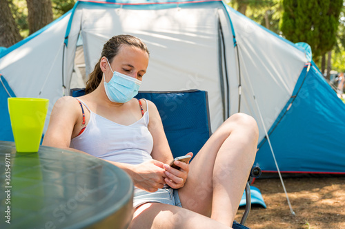 Woman wearing medical mask sitting in front of camping tent in a resort.