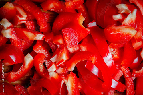 red fresh raw bell pepper chopped finely with a large knife on a wooden plate close-up top view