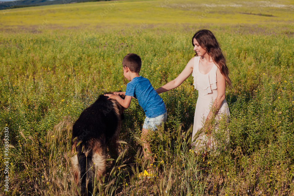 Mom and son walk with dog in yellow field