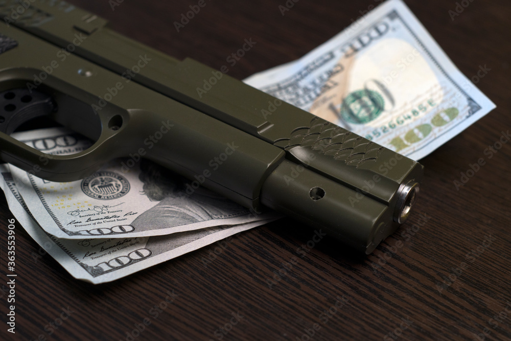 Khaki pistol and two hundred dollar bills lie on a wooden table. Close-up Khaki pistol and two hundred dollar bills lie on a wooden table. Close-up