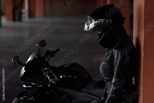 Horizontal shot of unrecognizable woman motorcycle rider driving her enduro motobike or chopper dressed in stylish leather clothes and protective equipment, blurred ligths and cars in background
