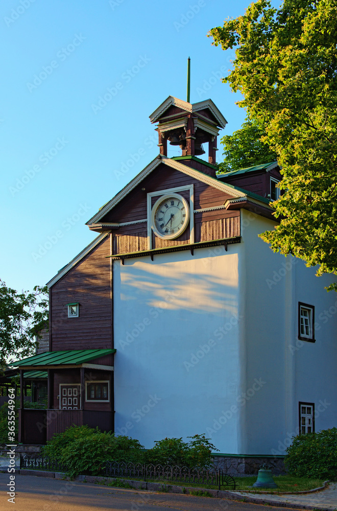 Obraz premium Scenic landscape view of the ancient clock tower during sunset. Decorated by carved wooden platbands. Trinity Monastery of St. Jonas. Blu sky background. Hryshko National Botanical Garden, Kyiv