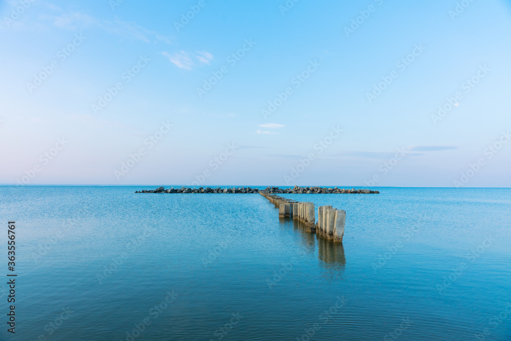Calm morning sea surface with old stone pier and rocks. Morning seascape.