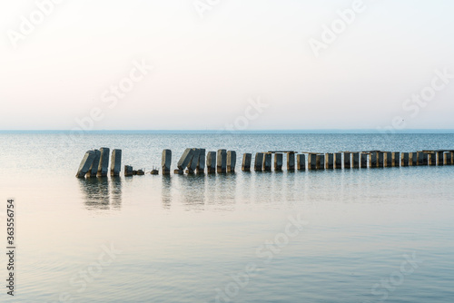 Calm morning sea surface with old stone pier and rocks. Morning seascape. © maxandrew