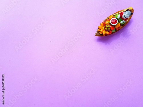 A traditional ceramic Thailand souvenir boat with fruit and a woman on a bright purple background.