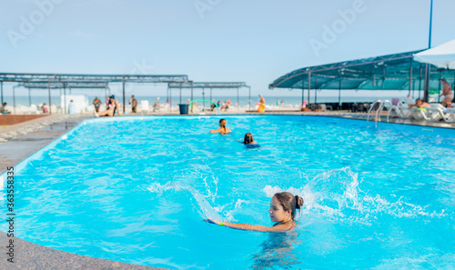 Top view unidentified pretty young girl happily splashing in blue clear water in the pool under the rays of bright sunlight. Concept of relaxation at the hotel and at sea. Advertising space