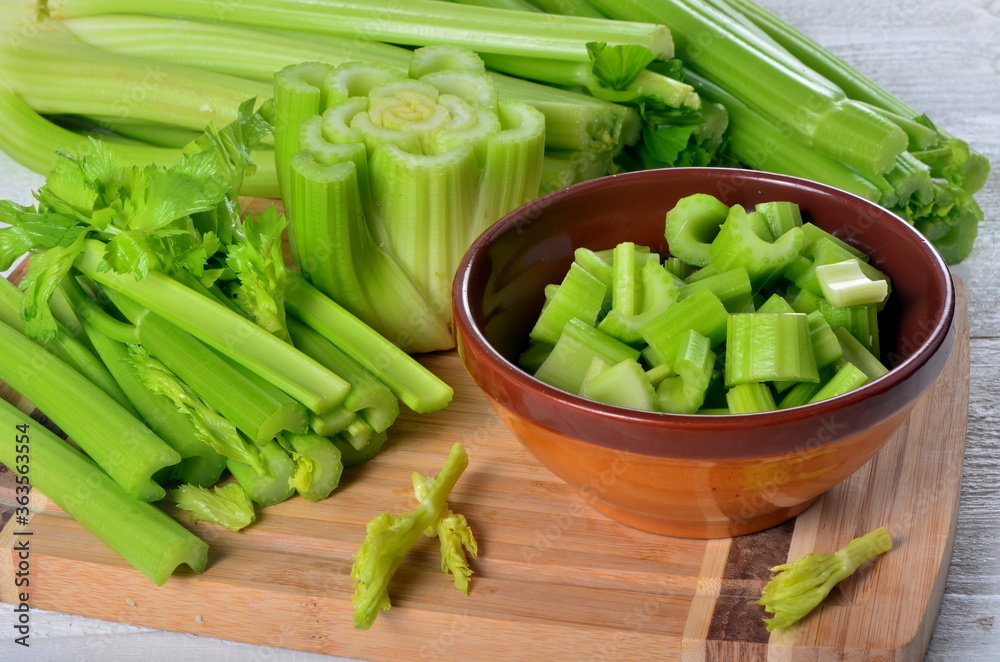 Sliced fresh celery in a clay bowl and Celery stalk on kitchen wooden board Sliced fresh celery in a clay bowl and Celery stalk on kitchen wooden board