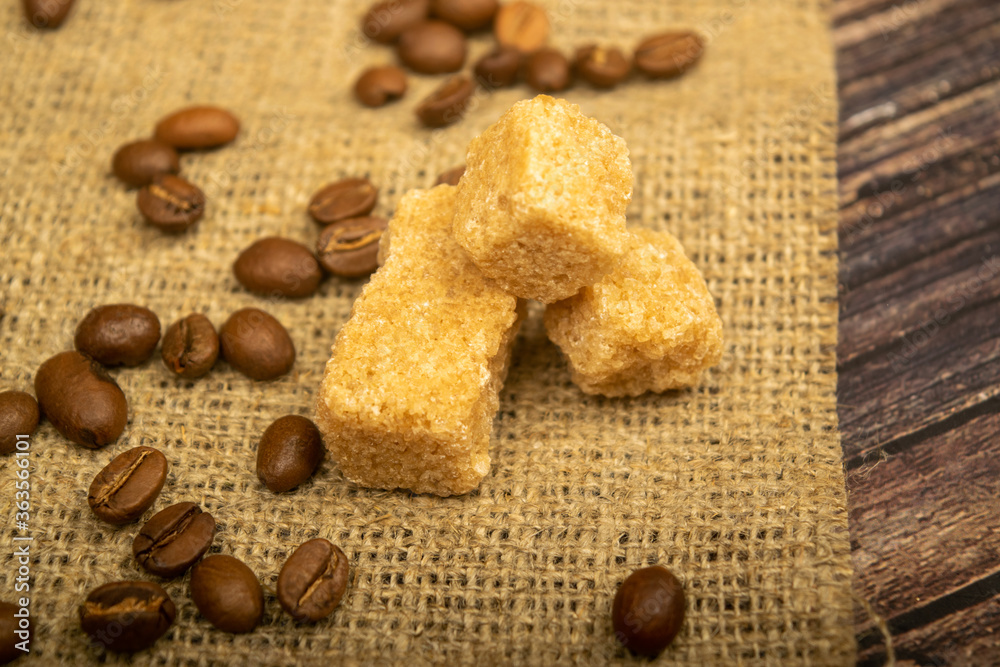 Coffee beans and pieces of brown sugar cane homespun fabric with a rough texture. Close up.