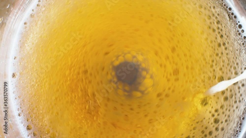 Close up flowing beer with bubbles. Whirlpool in the beer mixing by stirrer. Macro shooting, top view. Abstract background
