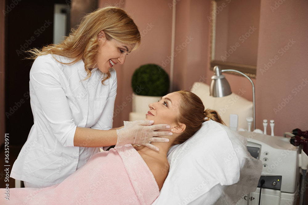 Beautician doctor inspects the face of a young woman before non-surgical rejuvenation procedure in a beauty clinic Beautician doctor inspects the face of a young woman before non-surgical rejuvenation procedure in a beauty clinic