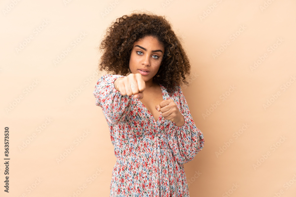 Young African American woman isolated on beige background with fighting gesture Young African American woman isolated on beige background with fighting gesture