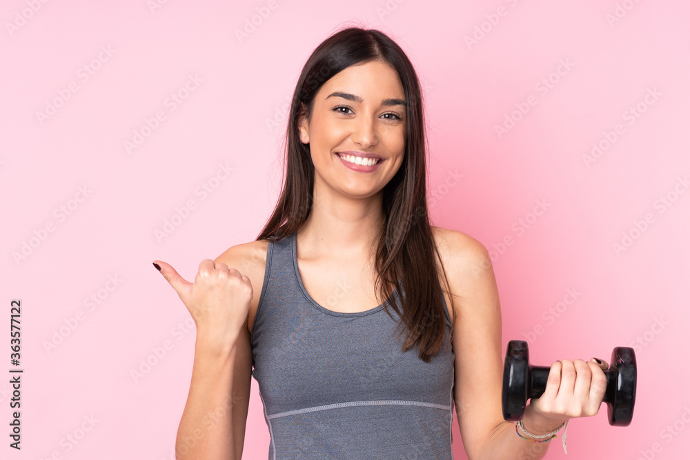 Young woman making weightlifting isolated on pink background pointing to the side to present a product Young woman making weightlifting isolated on pink background pointing to the side to present a product