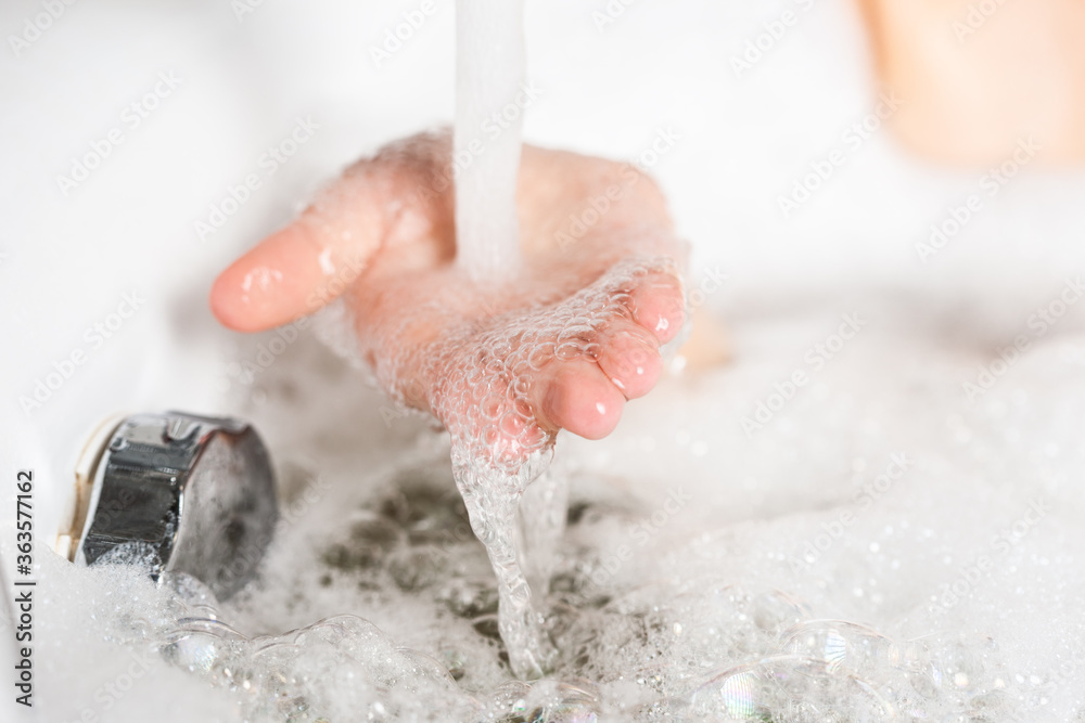 Fototapeta premium Close up female hand in soapy foam was substituted under the stream of water in the sink. Concept of cleanliness and hygiene during the coronovirus pandemic