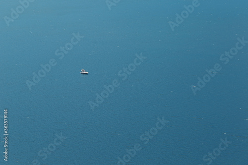 A yacht or a boat floats alone on the big water in sun glare. Open sea without wind.
