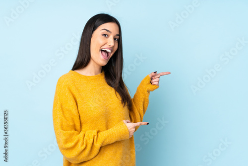 Young caucasian woman isolated on blue background surprised and pointing side
