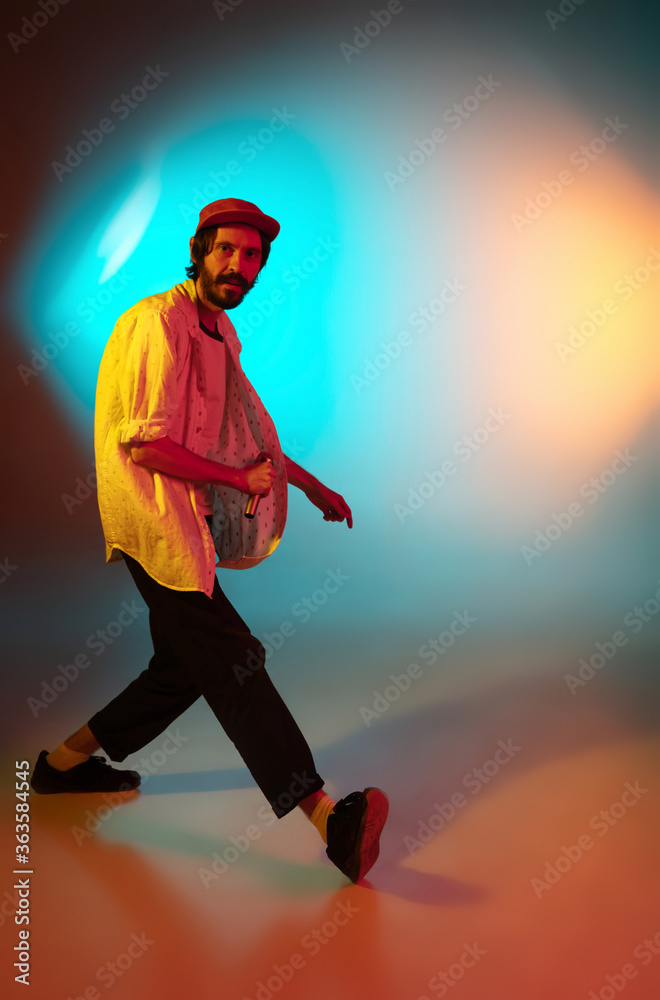 Dancing. Young inspired and expressive musician, singer performing on gradient colored background in neon light. Concept of music, hobby, festival, art. Joyful artist, colorful, bright portrait.