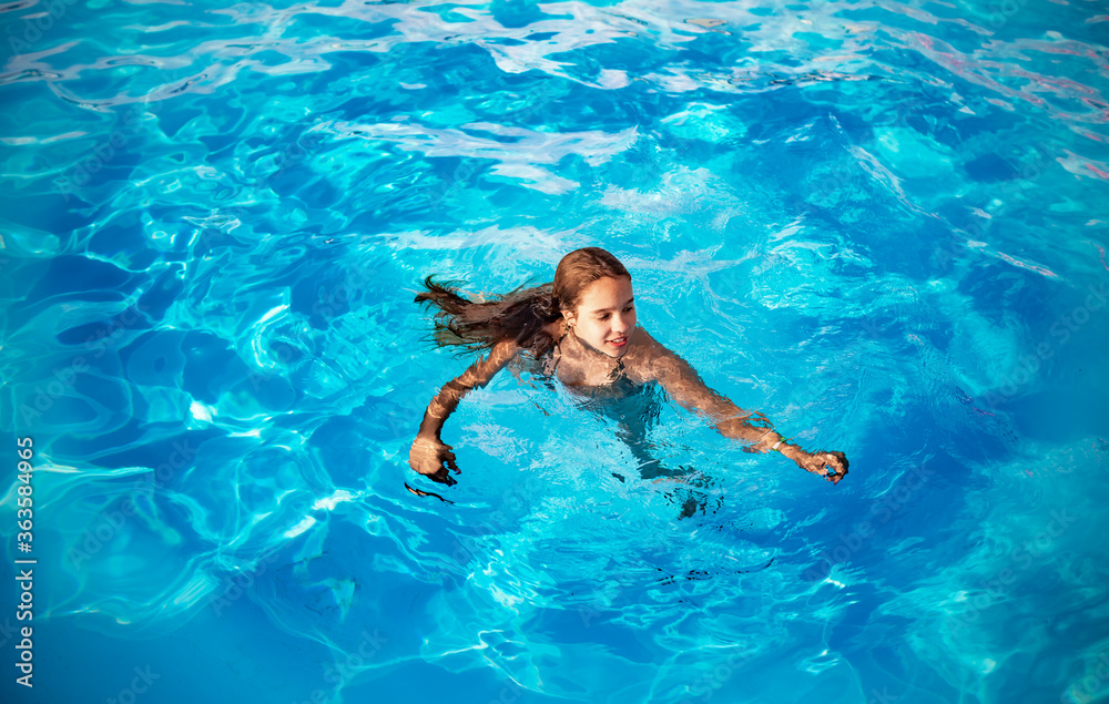 Teenage girl swims in the clear blue water of a pool during a vacation in a warm tropical country on a sunny warm summer day. Travel concept. Advertising space