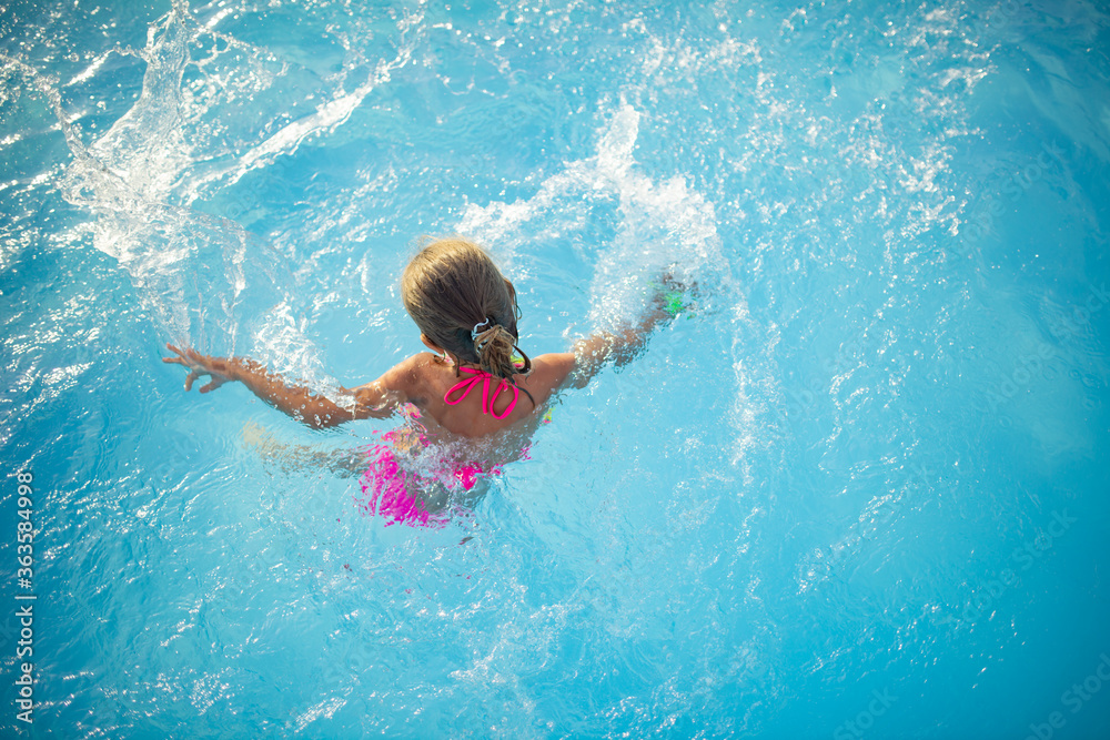 Top view happy little girl in bright color swimwear swims in the clear warm pool water Sunny summer day during vacation. Family vacation and tourism concept. Advertising space