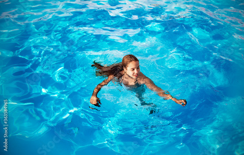 Teenage girl swims in the clear blue water of a pool during a vacation in a warm tropical country on a sunny warm summer day. Travel concept. Advertising space