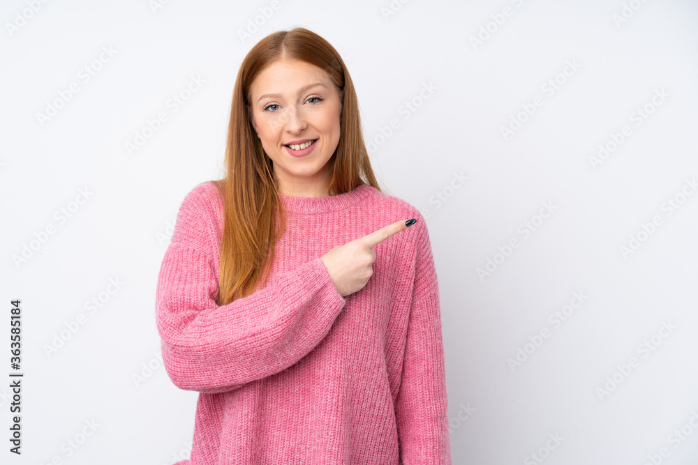 Young redhead woman with pink sweater over isolated white background pointing to the side to present a product Young redhead woman with pink sweater over isolated white background pointing to the side to present a product