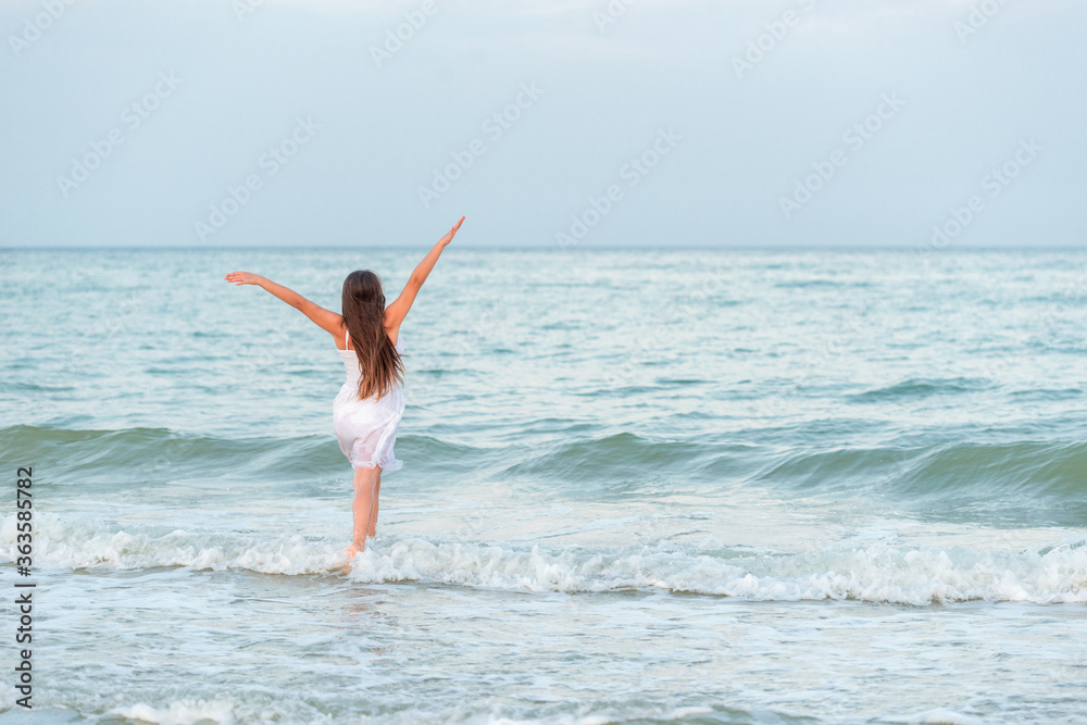 Girl happily spends time on the beach and walks along the sea waves on a sunny summer evening during vacation. Girl happily spends time on the beach and walks along the sea waves on a sunny summer evening during vacation.