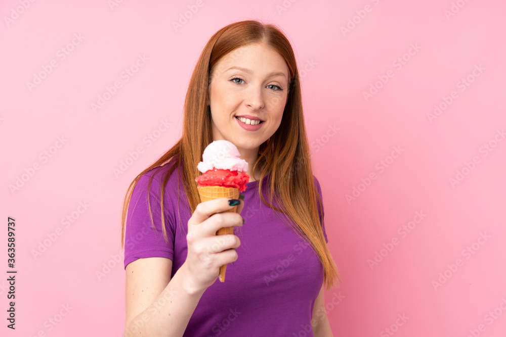 Young redhead woman with a cornet ice cream over isolated pink background with happy expression