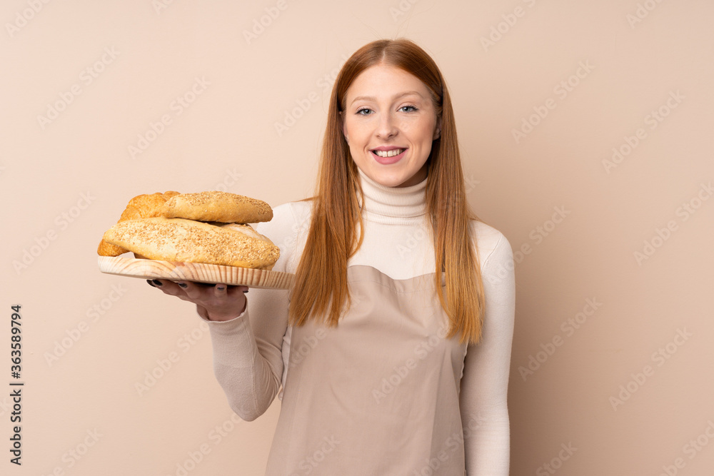 Young redhead woman in chef uniform. Female baker holding a table with several breads smiling a lot Young redhead woman in chef uniform. Female baker holding a table with several breads smiling a lot